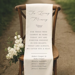 May include: White fabric runner with the text "In Loving Memory" and a small floral design. The text continues with "For those who cannot be here today, but are forever present in our hearts. Today and always, we saved you a seat."  The runner also lists the names "Robert Cooper Sr, Ruby Cooper, Beverly Saunders, Jerry L. Saunders, JonAnthony Page, Jerry E. Saunders".