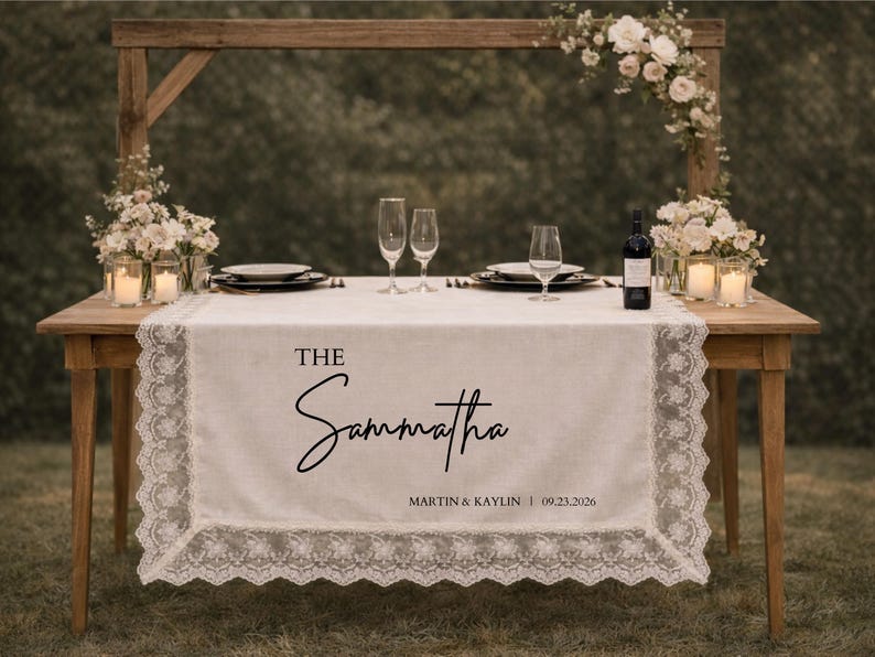 May include: A wooden table set for a wedding reception, with a white lace table runner bearing the name "Samantha" in black script. The table is adorned with flowers, candles, plates, glasses, and a bottle of wine.