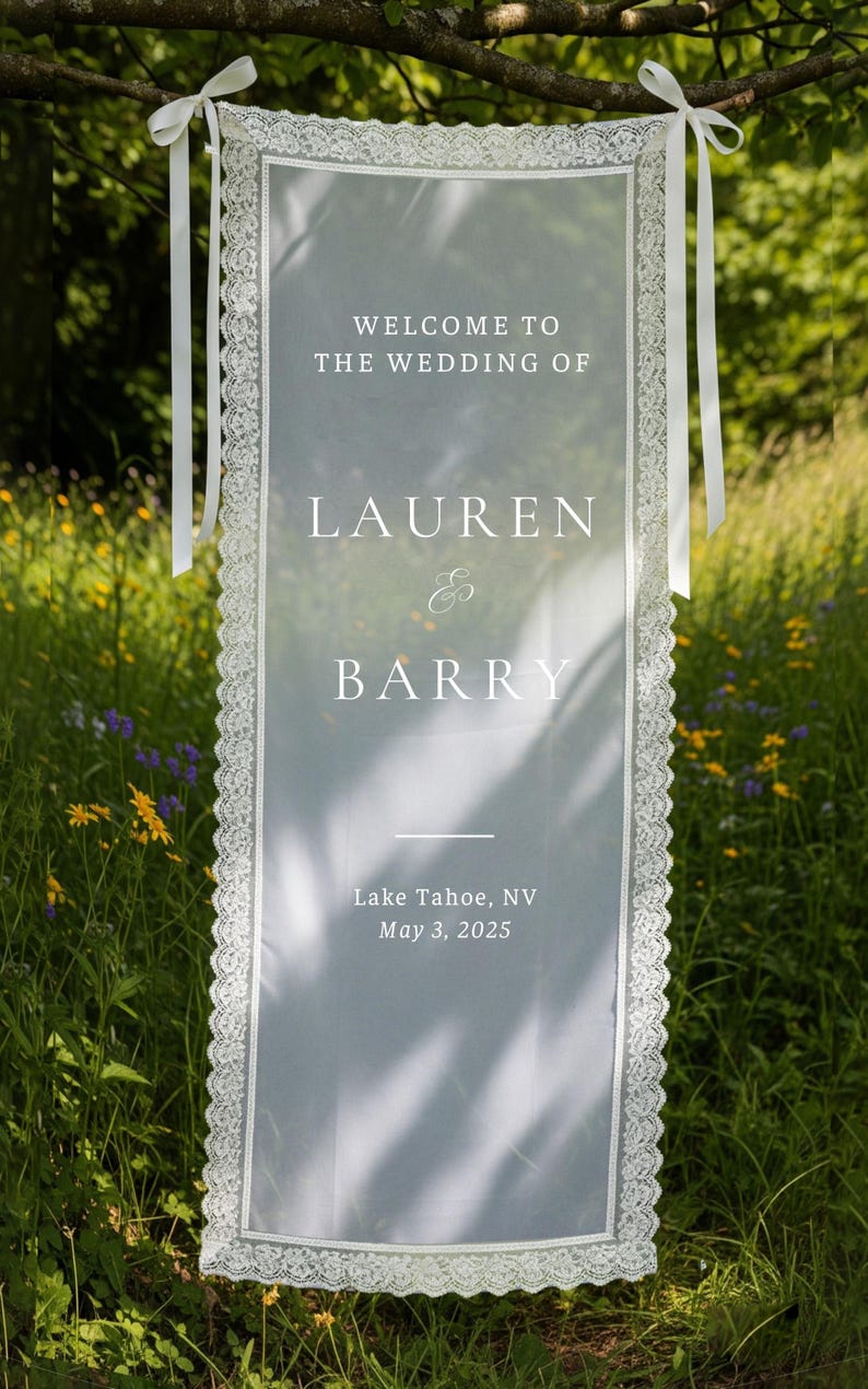 K&ouml;nnte beinhalten: Ein transparentes wei&szlig;es Hochzeitsbanner mit Spitzenbesatz und wei&szlig;en B&auml;ndern, das im Freien h&auml;ngt. Auf dem Banner steht "WELCOME TO THE WEDDING OF LAUREN & BARRY" und enth&auml;lt den Hochzeitsort und das Datum: Lake Tahoe, NV, 3. Mai 2025.