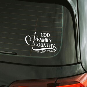 K&ouml;nnte beinhalten: Wei&szlig;er Vinyl-Aufkleber f&uuml;r ein Autofenster. Der Aufkleber zeigt die Worte "GOD FAMILY COUNTRY" in einer stilisierten Schriftart, mit einem Kreuz- und Herzsymbol. Der Satz "in that order" steht darunter.