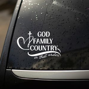 K&ouml;nnte beinhalten: Wei&szlig;er Vinyl-Aufkleber mit den Worten "GOD FAMILY COUNTRY" in einer stilisierten Schriftart, mit einem Kreuz- und Herz-Design. Der Satz "in that order" steht darunter. Der Aufkleber befindet sich auf einer schwarzen Oberfl&auml;che.