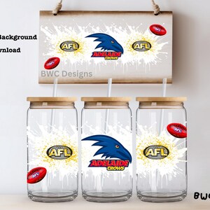 Könnte beinhalten: Drei Glasbecher mit Holzdeckeln und Strohhalmen, mit dem Logo des Adelaide Crows AFL-Teams. Das Design umfasst eine blaue Krähe, das AFL-Logo und einen roten Football vor einem weißen Spritzer-Hintergrund. Ein Schild mit dem gleichen Design hängt darüber.