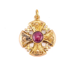 May include: A gold cross pendant featuring a textured, ornate surface with intricate filigree-like detailing. At the center of the cross is a single, round, polished magenta-colored gemstone. The pendant includes a small circular bail at the top.
