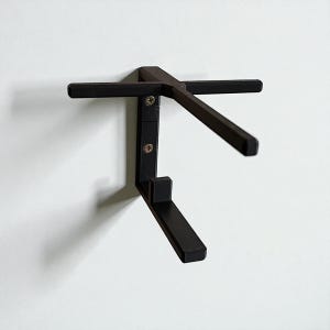 Puede incluir: Estante de pared de metal negro con un dise&ntilde;o &uacute;nico. El estante tiene un soporte vertical con dos brazos horizontales y un soporte inferior en &aacute;ngulo. Se fija a una pared blanca con tornillos.