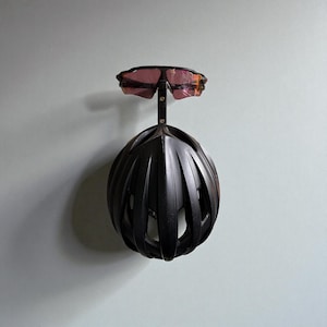Puede incluir: Un casco de bicicleta negro con gafas de sol rosas adjuntas. El casco es negro mate con m&uacute;ltiples aberturas. Las gafas de sol est&aacute;n montadas encima del casco, creando un aspecto deportivo y aerodin&aacute;mico.
