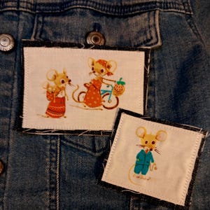 May include: A denim jacket with three embroidered patches featuring cartoon mice. One patch shows two mice, and another shows a single mouse in a blue suit. The patches are rectangular with black borders.