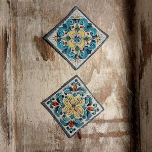 May include: Two decorative ceramic tiles with a blue, yellow, and red floral pattern are displayed in a wooden frame.