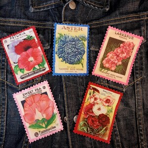 May include: Five rectangular fabric patches with scalloped edges, each featuring vintage botanical seed packet illustrations of Petunia, Aster, Larkspur, Sweet Pea, and Single Pinks, arranged on a dark blue denim jacket with visible metal buttons.
