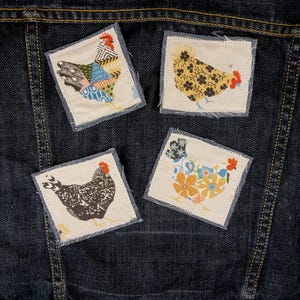 May include: A dark blue denim jacket featuring four square fabric patches sewn onto the back. Each patch displays a different chicken illustration, including one with geometric patterns, one with floral prints, one with a speckled design, and one with flowers.