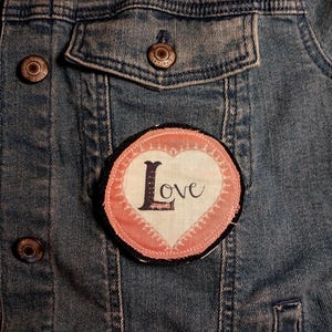 May include: A denim jacket with a pink and white heart-shaped patch that says "Love" in black script.