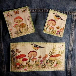 May include: Three rectangular fabric patches featuring botanical illustrations of mushrooms, birds, and butterflies on a cream background with a light green gingham border, attached to a blue denim fabric surface.