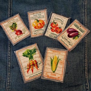 May include: A collection of fabric patches featuring vintage-style illustrations of vegetables. The patches include images of beets, a pumpkin, tomatoes, eggplant, carrots, and corn, with text such as "Vegetables" and "Farmers Market."