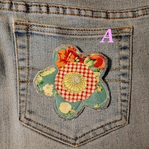 May include: A blue denim jean pocket with a colorful fabric flower applique. The flower is made of red, white, green, and yellow fabric.