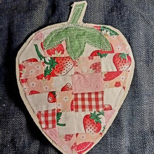 以下が含まれることがあります： イチゴの形をした布製のワッペン。イチゴ、ギンガムチェック、小花柄など、赤、ピンク、白の様々なパッチワークデザインが施されています。上部には緑色の布製の葉が付いており、周囲はステッチで縁取られています。