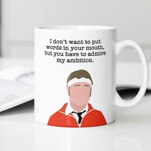 May include: White ceramic mug with a red and white illustration of a person wearing a headband and a red jacket. The mug has a black text that reads "I don't want to put words in your mouth, but you have to admire my ambition."
