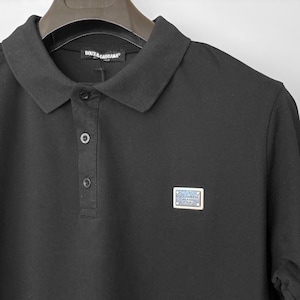 Puede incluir: Polo negro con cuello y tres botones. La camisa tiene un pequeño logotipo rectangular en el pecho. La marca "Dolce & Gabbana" es visible en el cuello.