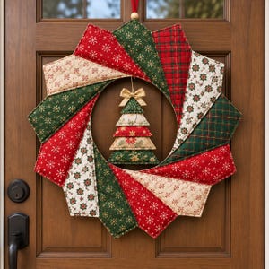 May include: A quilted fabric wreath featuring alternating triangular segments in red, dark green, and cream with snowflake, plaid, and floral patterns. A small, tiered, stuffed fabric Christmas tree ornament with a gold bow hangs in the center.
