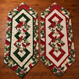 May include: Two hexagonal table runners featuring a festive holiday print. One runner has a dark green border, while the other has a red border. Both display a central pattern of red cardinals, holly berries, green leaves, and gold snowflakes.