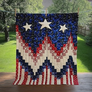 May include: A patriotic quilt with a design reminiscent of the American flag. The quilt features a blue background with white stars, red and white stripes, and a patchwork pattern. The quilt is hanging on a clothesline outdoors.