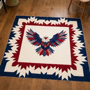 May include: A square quilt featuring a central applique of a bald eagle with wings spread wide. The eagle is constructed from red, white, and blue fabric with star and stripe patterns. The border consists of a jagged, star-like geometric design.