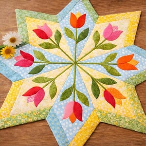 May include: A star-shaped quilted placemat featuring a floral design. The placemat has a light blue center with white polka dots, surrounded by yellow and green sections. Red, pink, and orange tulip appliqués with green leaves are arranged around the center.