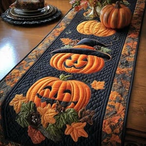 May include: A black Halloween table runner with orange pumpkin and leaf appliqués. The runner features three smiling jack-o'-lanterns, a witch's hat, and autumn leaves. The runner is placed on a wooden table, perfect for fall decor.