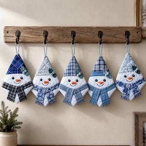 May include: Five quilted snowman ornaments hanging from a wooden rack. Each snowman features a unique blue and white patterned hat, a white face with black eyes, an orange carrot nose, and a blue or grey scarf with green holly leaf accents.
