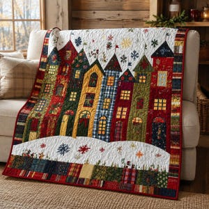 May include: A quilted throw blanket featuring a row of colorful houses in red, green, yellow, and blue with lit windows. The design includes a white snowy foreground with embroidered snowflakes and a border made of various plaid and floral fabric patches.