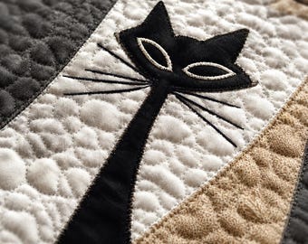 May include: A quilted fabric panel featuring a black cat appliqué with embroidered eyes and whiskers. The background consists of white, gray, and tan fabric sections with a stippled, pebble-like texture created by dense machine quilting stitches.
