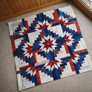 May include: A handmade quilt with a patriotic theme. The quilt features a star pattern in the center, surrounded by squares in red, white, and blue. The quilt is made of fabric and is likely used for bedding or decoration.