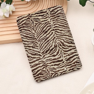 May include: A rectangular electronic reader cover featuring a dark brown and cream-colored zebra stripe pattern. The cover has rounded corners and a smooth, flat surface that displays the animal-inspired print across the entire front panel.