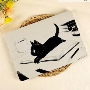 Könnte beinhalten: Eine Laptop-Hülle mit einer Illustration einer schwarzen Katze. Die Katze liegt auf einem offenen Buch, mit einer Kaffeetasse, einem Tintenfass und Büchern im Hintergrund. Das Design ist in Schwarz und Weiß gehalten.