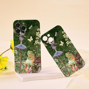 Puede incluir: Dos fundas verdes para teléfono con un diseño caprichoso. Las fundas presentan un hada de pie sobre una seta, una rana, mariposas y flores. El fondo es verde oscuro con flores blancas y libélulas.