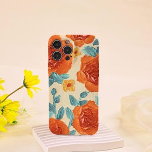 May include: A phone case with a floral design. The case features orange roses, yellow flowers, and blue leaves on a cream background. The case has a raised texture and a camera cutout.