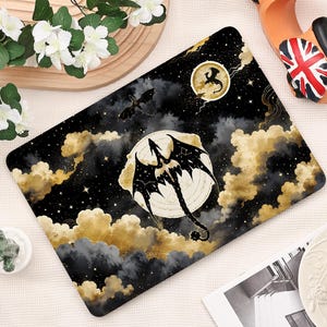 May include: A rectangular laptop skin featuring a black night sky filled with gold clouds, stars, and two silhouettes of dragons. One dragon is centered in front of a large, pale moon, while a smaller dragon silhouette appears near a second moon.