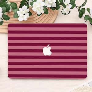 May include: A laptop case with a horizontal striped pattern in shades of burgundy and pink. The Apple logo is centered on the case. The case is rectangular and appears to be made of a smooth material.