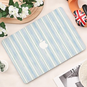 Puede incluir: Una funda para portátil con un diseño de rayas azules y blancas. Tiene un logotipo blanco de Apple en el centro. Las rayas son verticales y tienen un efecto acuarela. La funda está sobre una superficie blanca.
