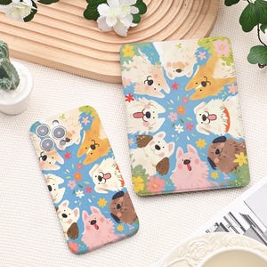 Peut inclure: Une coque de téléphone et un carnet avec un motif répété de chiens de dessin animé de différentes couleurs, sur un fond bleu clair avec des fleurs colorées. La coque du téléphone a une découpe pour l'appareil photo. Le carnet est rectangulaire.