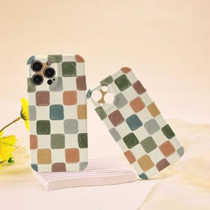 May include: Two phone cases with a cream background and a repeating pattern of colourful squares in shades of brown, green, blue, and orange. One case is upright, the other is leaning against it.