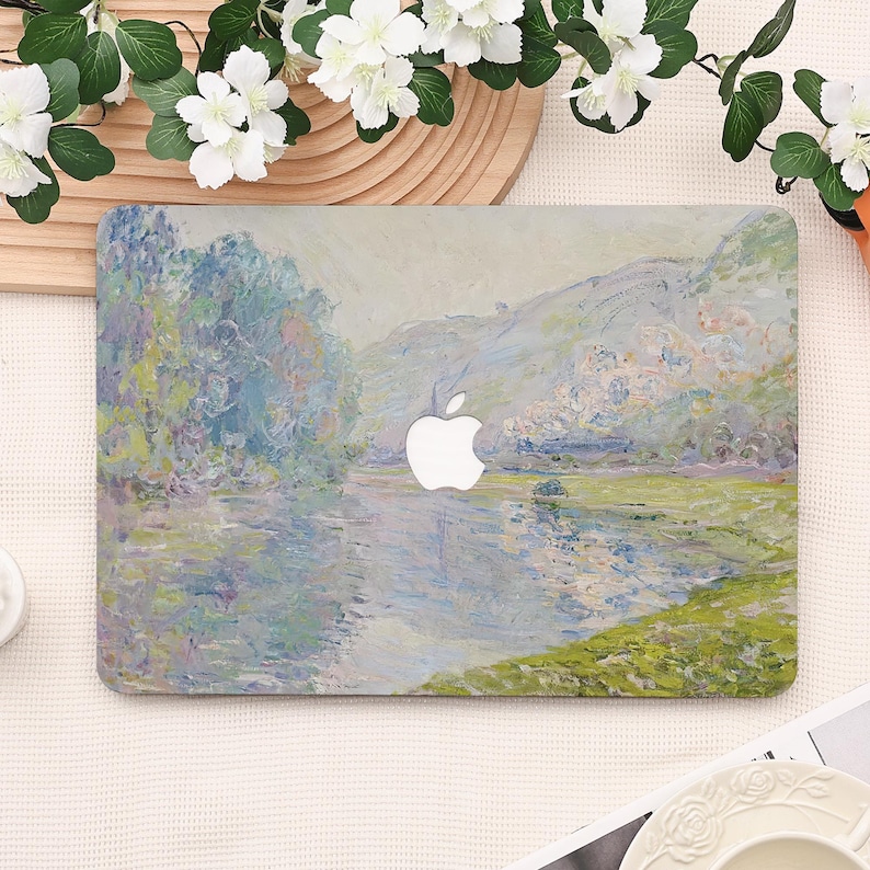 Pode incluir: Uma capa para laptop com uma pintura de paisagem em tons de azul, verde e branco, que lembra o impressionismo. A capa tem um logotipo branco da Apple e uma vista fluvial com &aacute;rvores e montanhas.