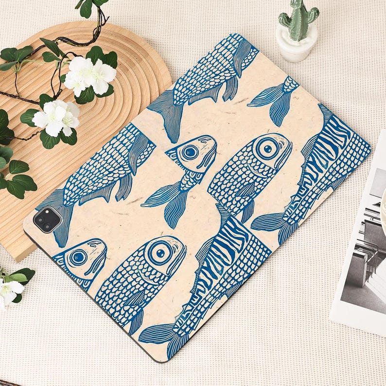 May include: A tablet case featuring a repeating pattern of blue fish illustrations on a beige background. The fish have detailed scales and fins, creating a nautical theme. The case is rectangular and designed to fit a tablet.