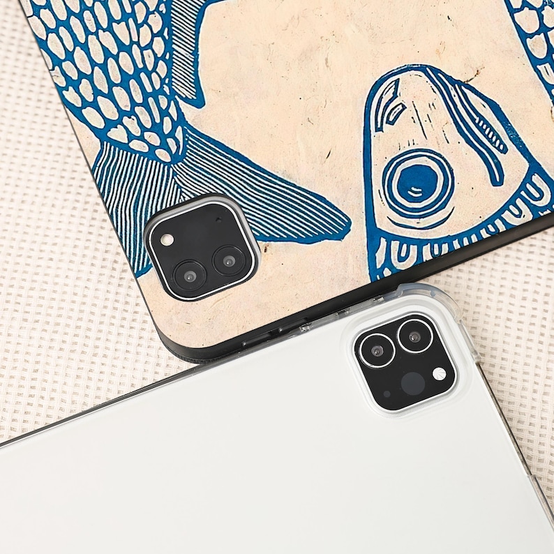 May include: Two tablet cases. One case features a blue fish design on a beige background. The other case is white. Both cases have a camera cutout with two lenses.