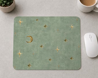 Peut inclure: Un tapis de souris rectangulaire avec un fond texturé vert sauge présentant un motif d'éléments célestes dorés, incluant un croissant de lune avec un visage et diverses étoiles à quatre branches de tailles variées dispersées sur la surface.