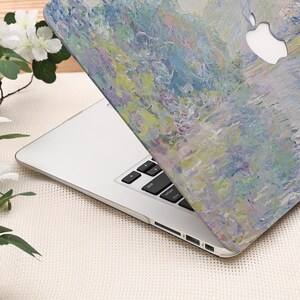 Pode incluir: Um laptop prateado com uma capa com um design de pintura impressionista em tons de azul, verde e amarelo. O logotipo da Apple &eacute; vis&iacute;vel. O teclado &eacute; preto. O design evoca uma cena aqu&aacute;tica.