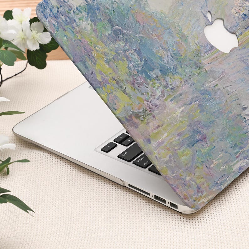 Pode incluir: Um laptop prateado com uma capa com um design de pintura impressionista em tons de azul, verde e amarelo. O logotipo da Apple &eacute; vis&iacute;vel. O teclado &eacute; preto. O design evoca uma cena aqu&aacute;tica.