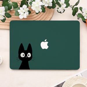 May include: A dark green laptop cover with a black cat illustration and white eyes and whiskers. The Apple logo is on the right. The cover is rectangular and has a smooth surface.