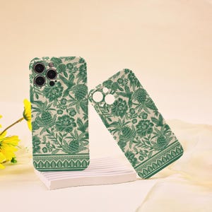 May include: Two green and white floral phone cases for an iPhone 13 Pro Max. The cases feature a vintage floral pattern with a green and white colour scheme.