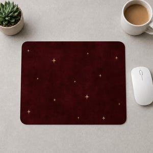 May include: A rectangular mouse pad featuring a deep burgundy, textured background adorned with a scattered pattern of small, four-pointed gold stars. The surface has a matte finish, and the design is consistent across the entire rectangular area.