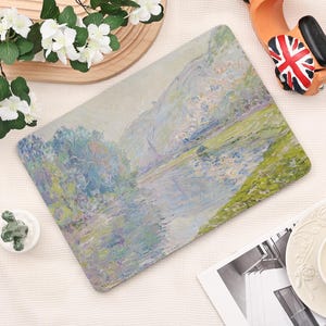 Pode incluir: Tapete de rato retangular com uma pintura de paisagem impressionista com um rio e montanhas. A obra de arte utiliza azuis, verdes e brancos, criando uma est&eacute;tica serena. O tapete &eacute; projetado para uso em computador.