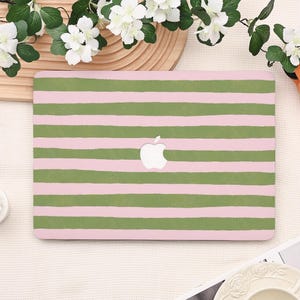 May include: A pink laptop case with horizontal green stripes. The Apple logo is visible in the center. The case is rectangular and appears to be made of a hard, protective material. The design is simple and modern.